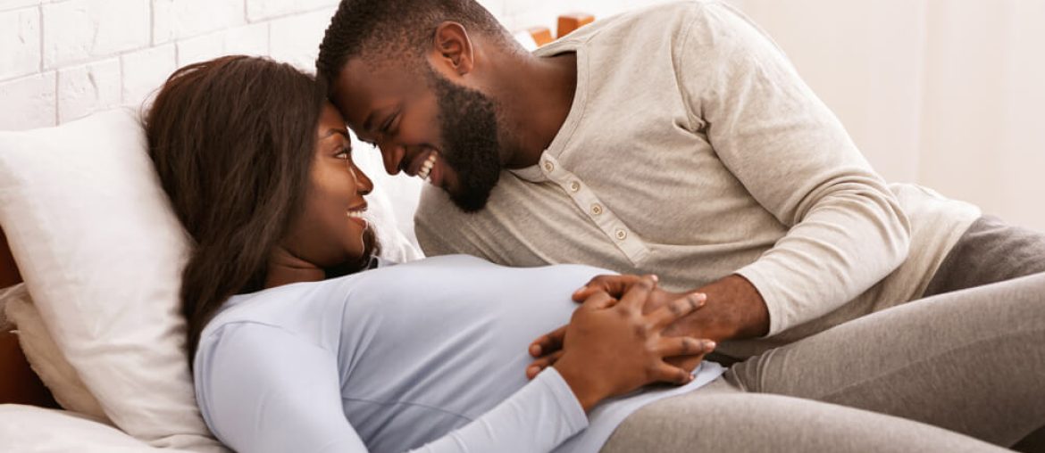 Pregnant couple in love cuddling in bed