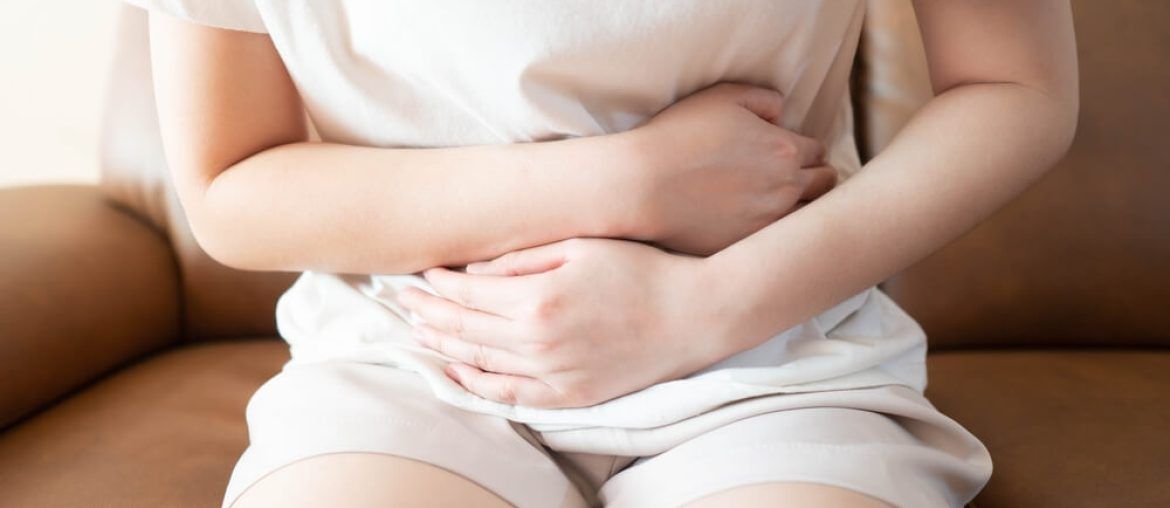 Young female suffering form stomach ache while sitting on couch at home