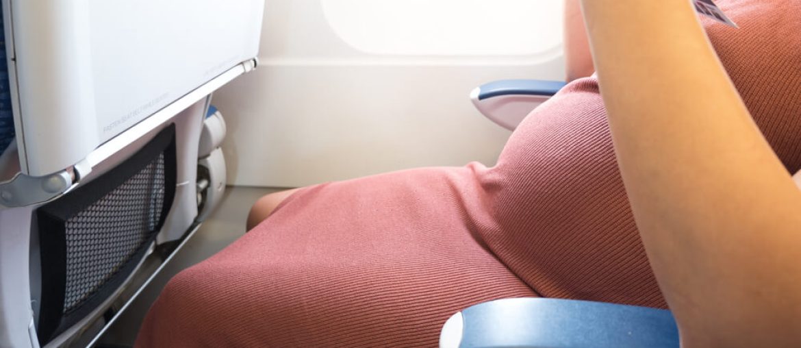 Happy pregnant woman is traveling to destination by plane sitting and reading book