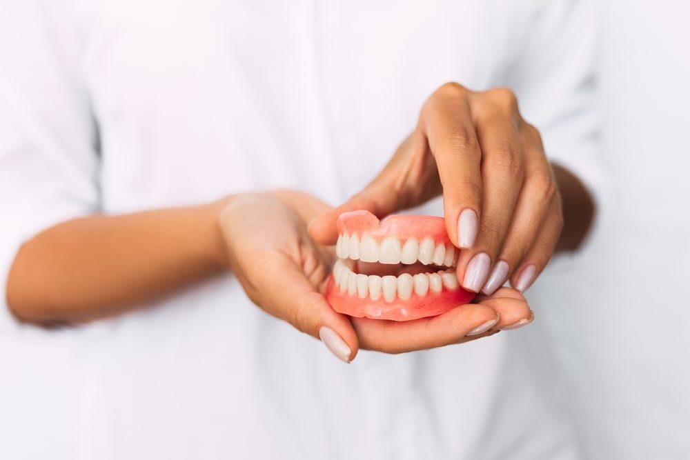 The dentist is holding dentures in his hands