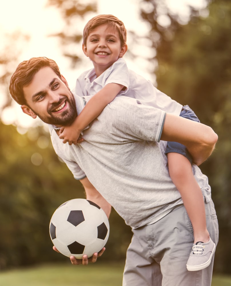 Handsome dad with his little cute sun are having fun and playing football on green grassy lawn