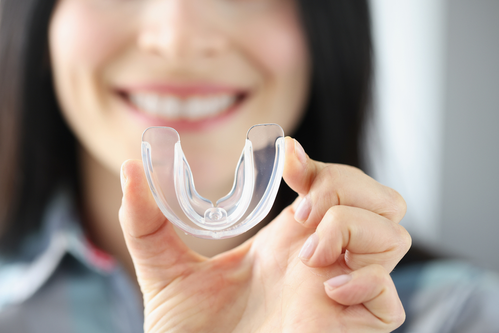 A woman holding an example of Bite Guards while smiling