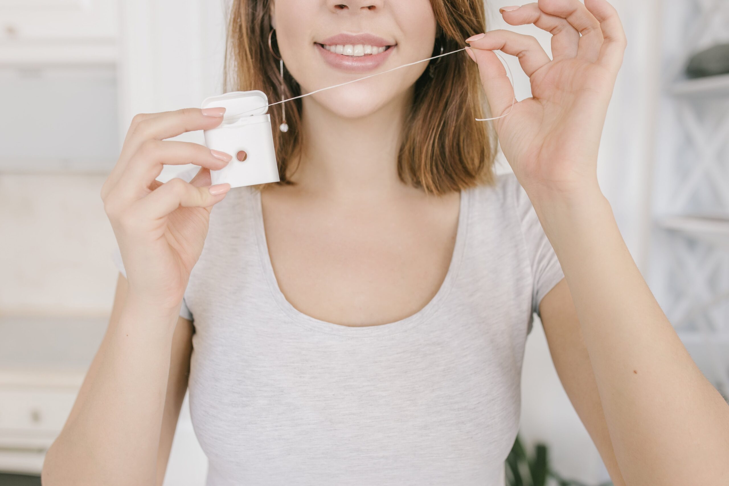 lower half of woman's smiling face as she pulls out dental floss