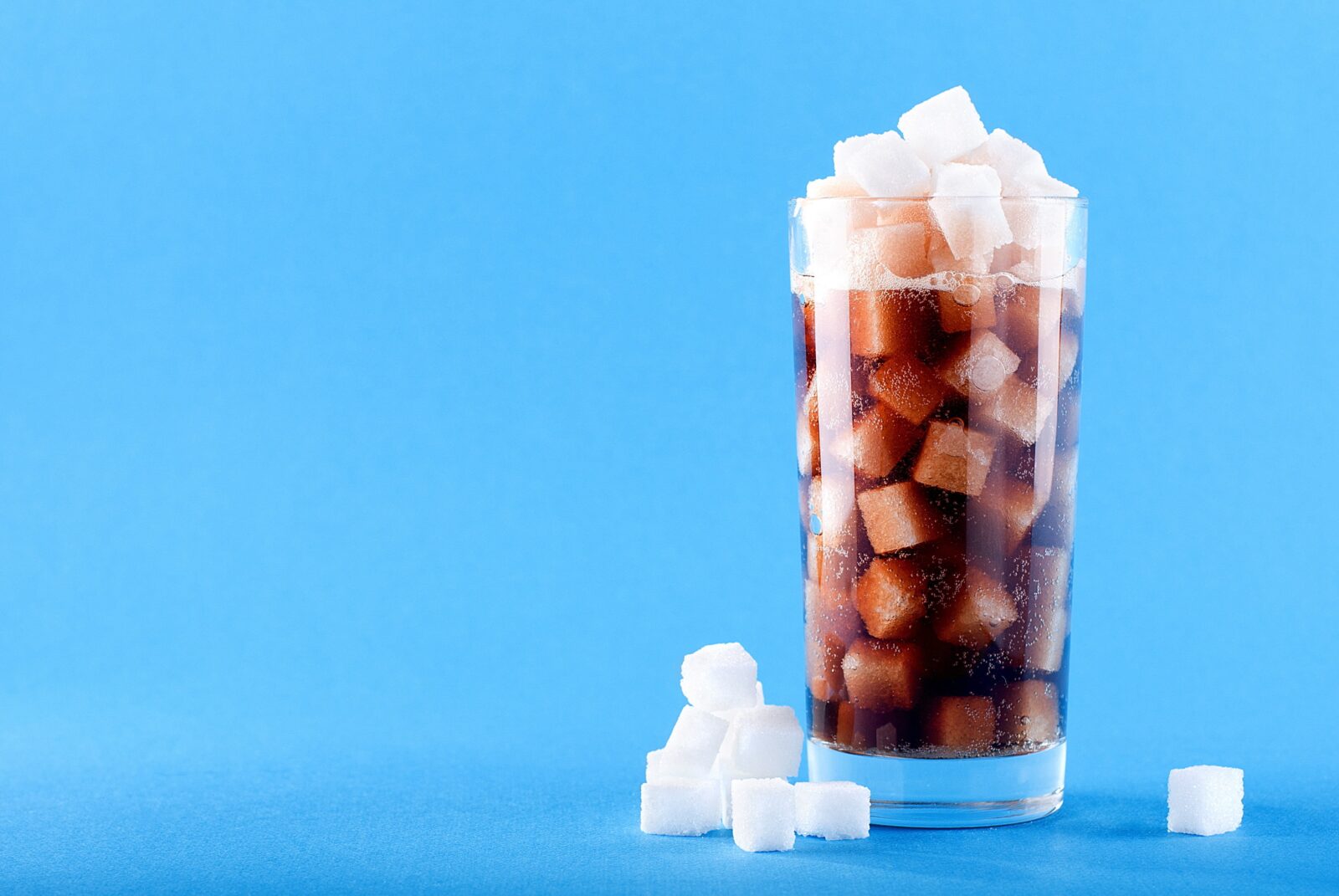 glass of dark cola overflowing with sugar cubes