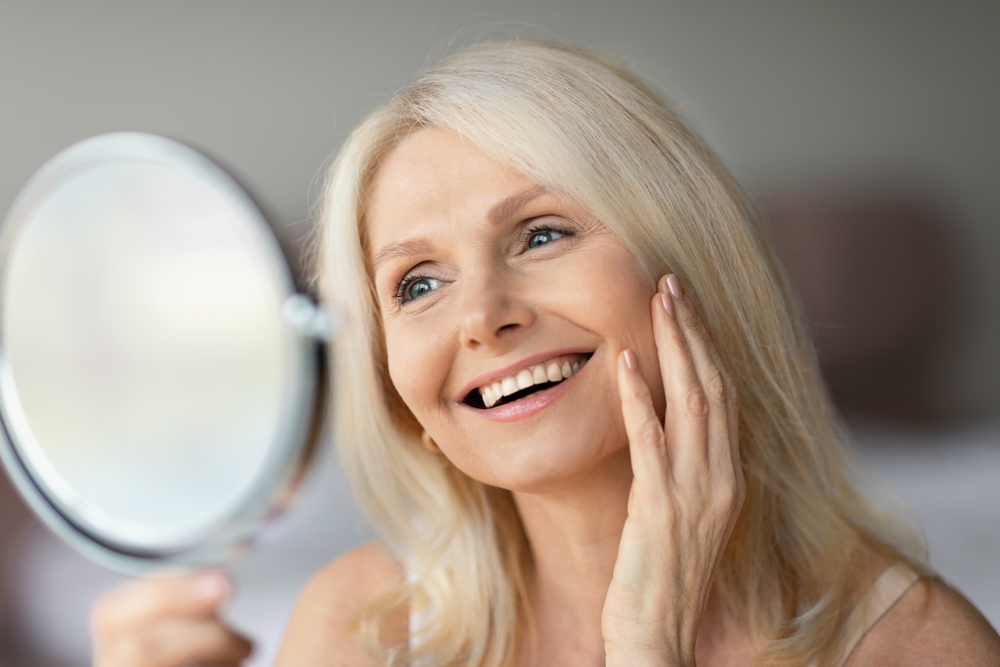 Portrait of beautiful senior woman looking in miror and touching face, checking her wrinkles and smiling