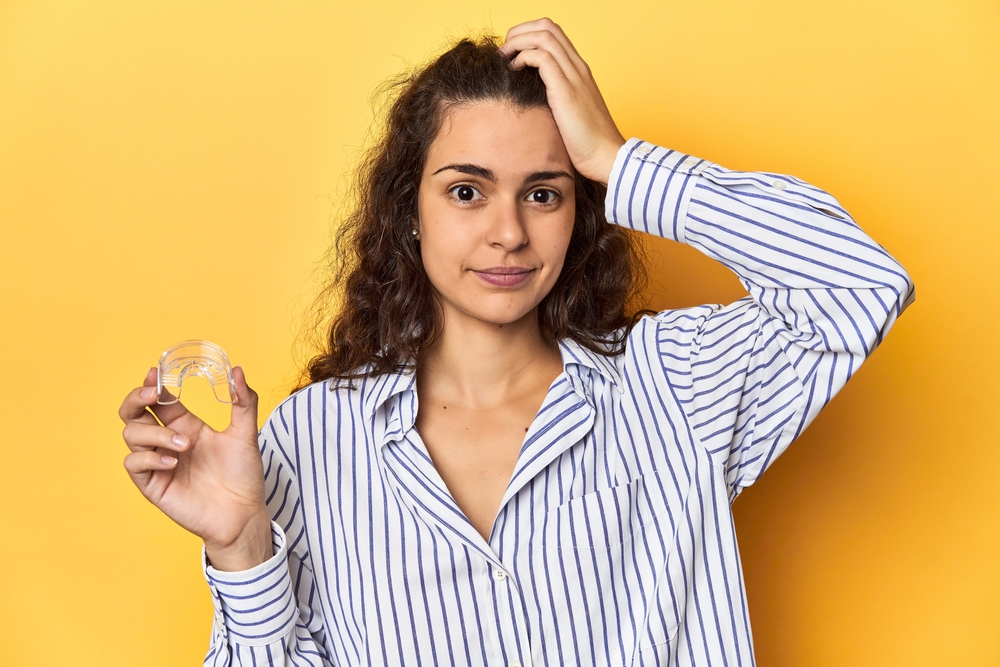 A woman is holding an invisible teeth corrector, looking shocked