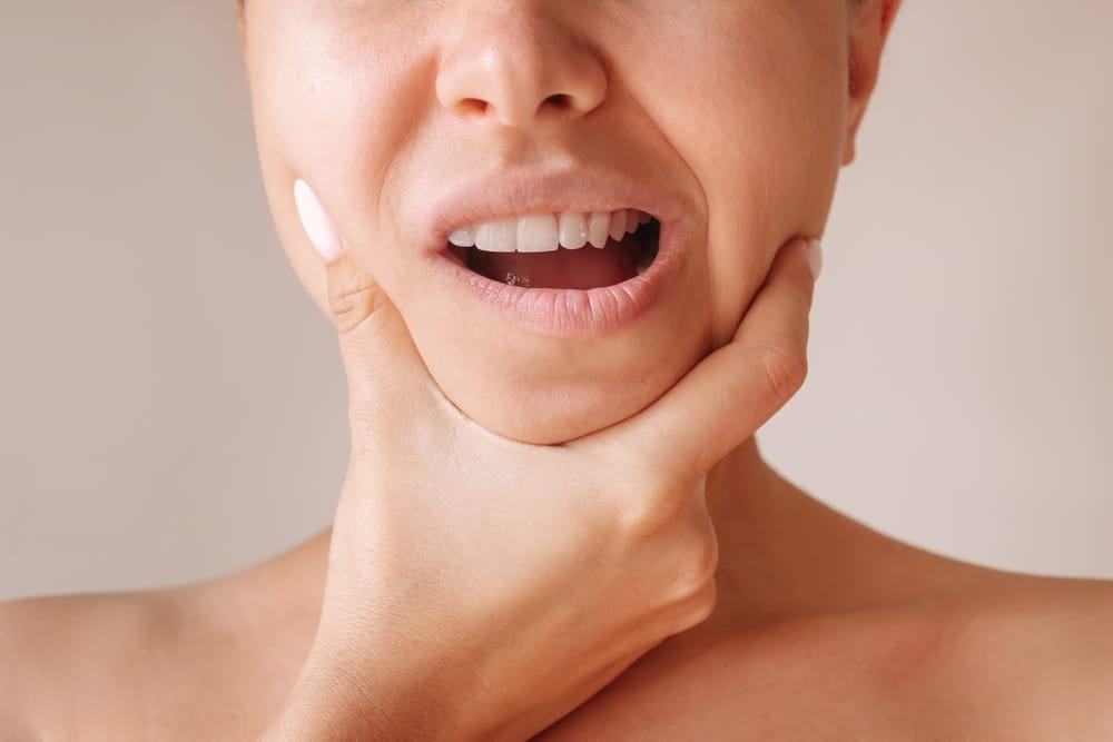 Cropped shot of a young woman suffering from jaw pain holding her chin isolated on a beige background