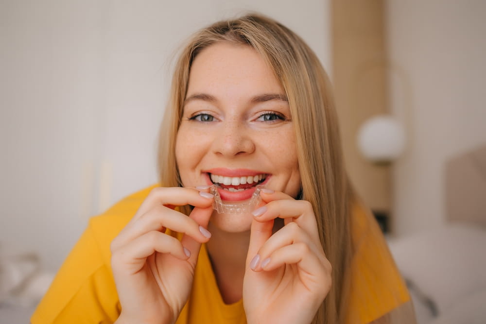 Young woman holding and using a clear aligner, promoting dental care