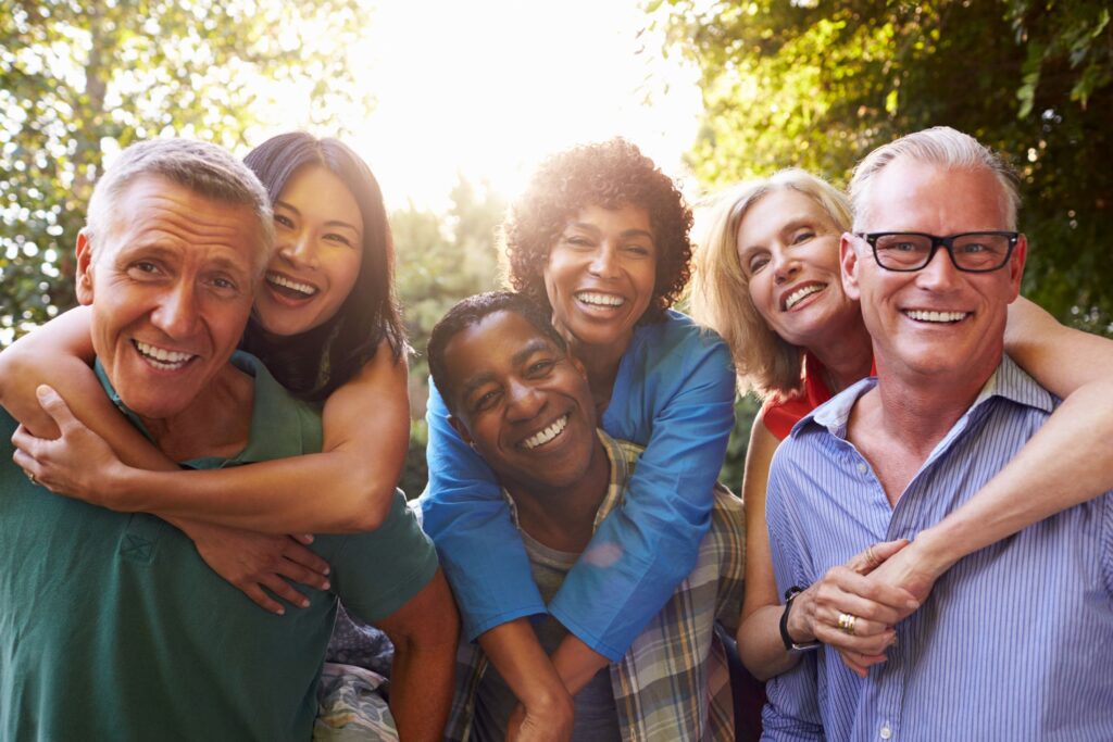 Mature Friends Giving Piggybacks In Backyard Together