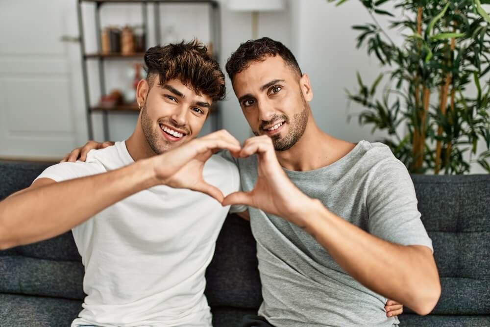 Two hispanic men couple smiling confident doing heart shape with hands at home