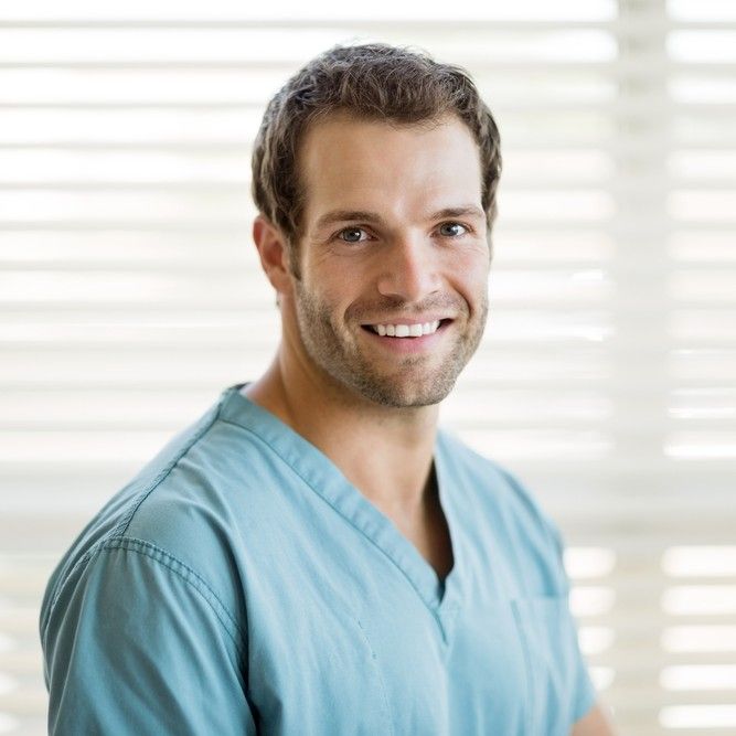 Portrait of happy young male nurse in scrubs at clinic