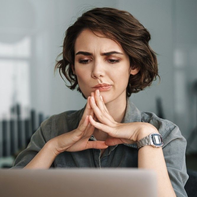 Image of young beautiful brooding woman working with laptop while sitting at table in office