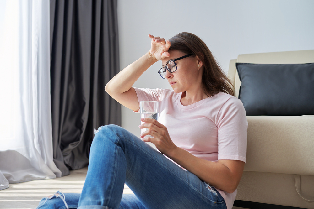 Serious sad middle aged mature woman sitting at home holding glass