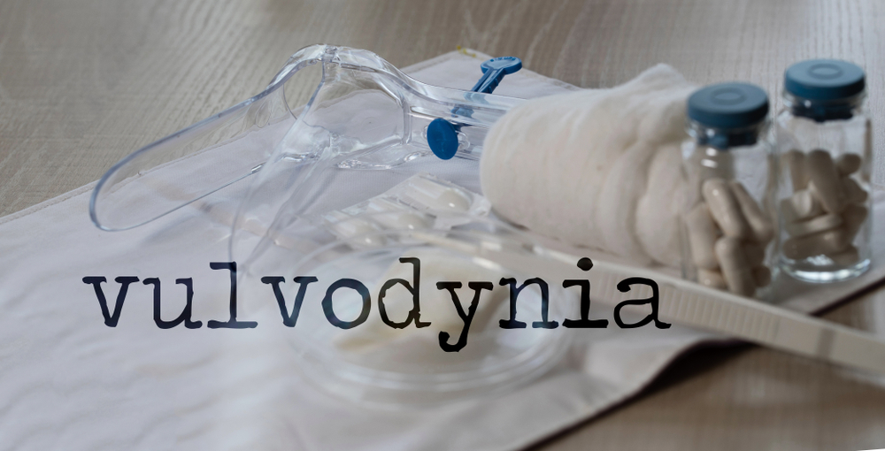 Word VULVODYNIA. Plastic vaginal speculum, pills and other tools in the background. Closeup