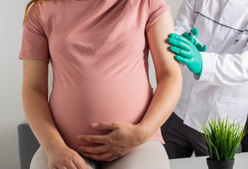 A doctor in medical gloves vaccinates a pregnant girl against flu, covid and whooping cough. Infection