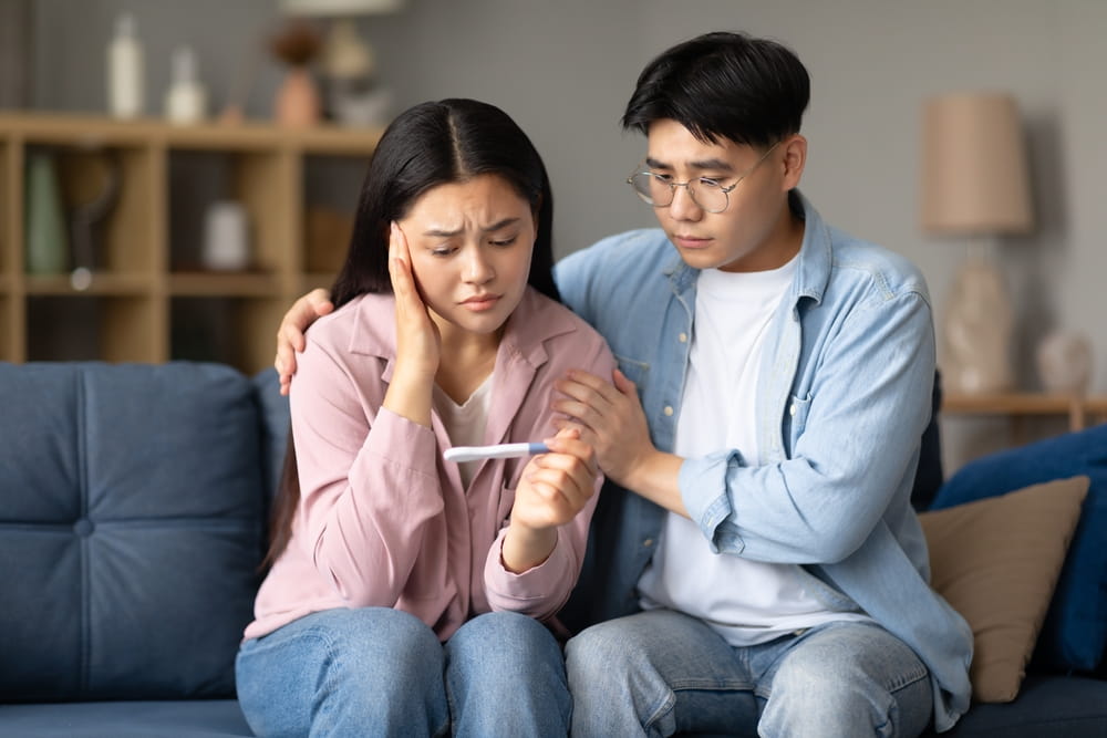 Depressed Korean Couple Holding Negative Pregnancy Test