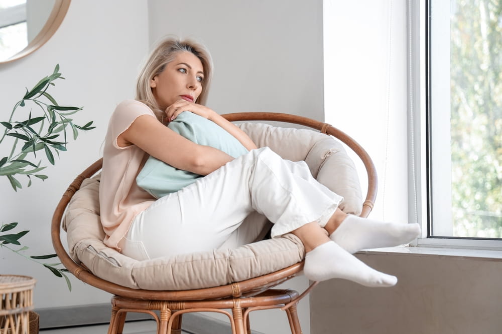 Sad mature woman experiencing menopause in armchair at home