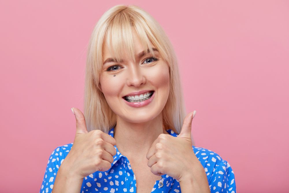 woman with blonde hair gesturing thumb up while pointing finger at braces