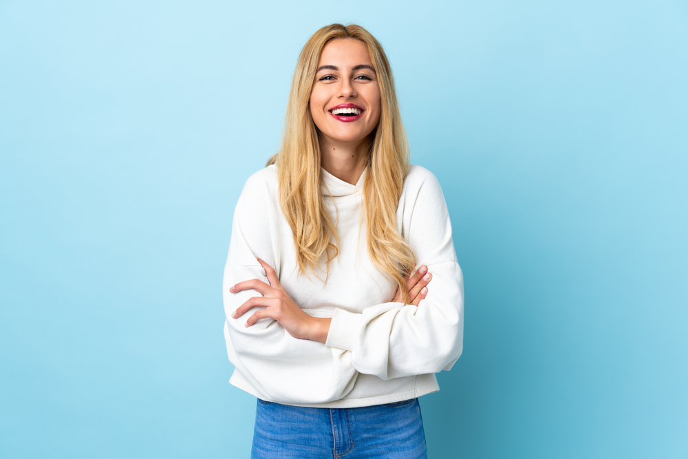 blonde woman over isolated blue background keeping the arms crossed