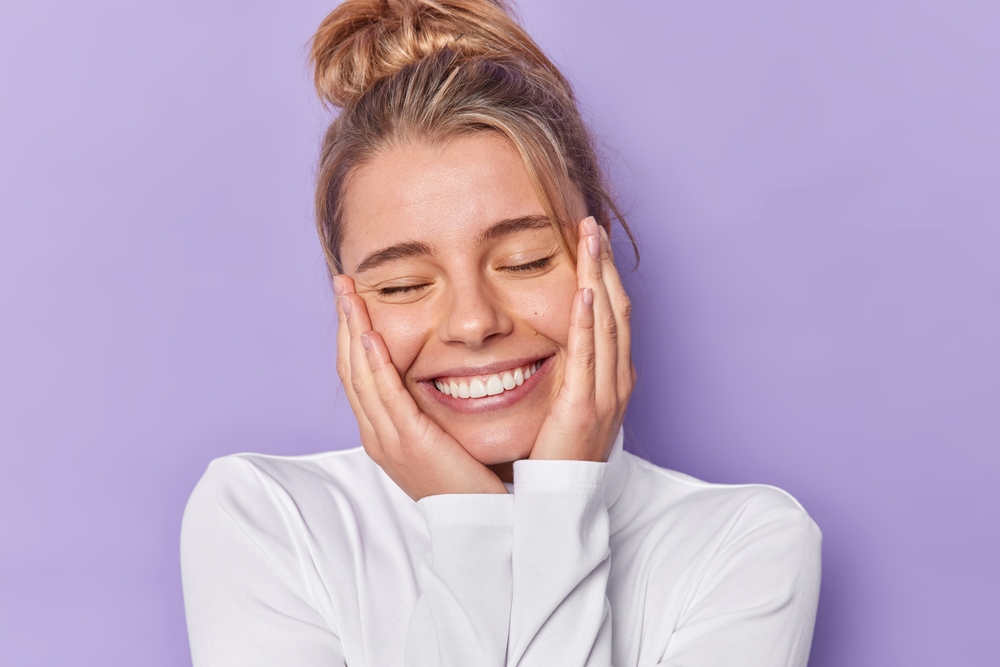 Cheerful woman keeps eyes closed smiles broadly