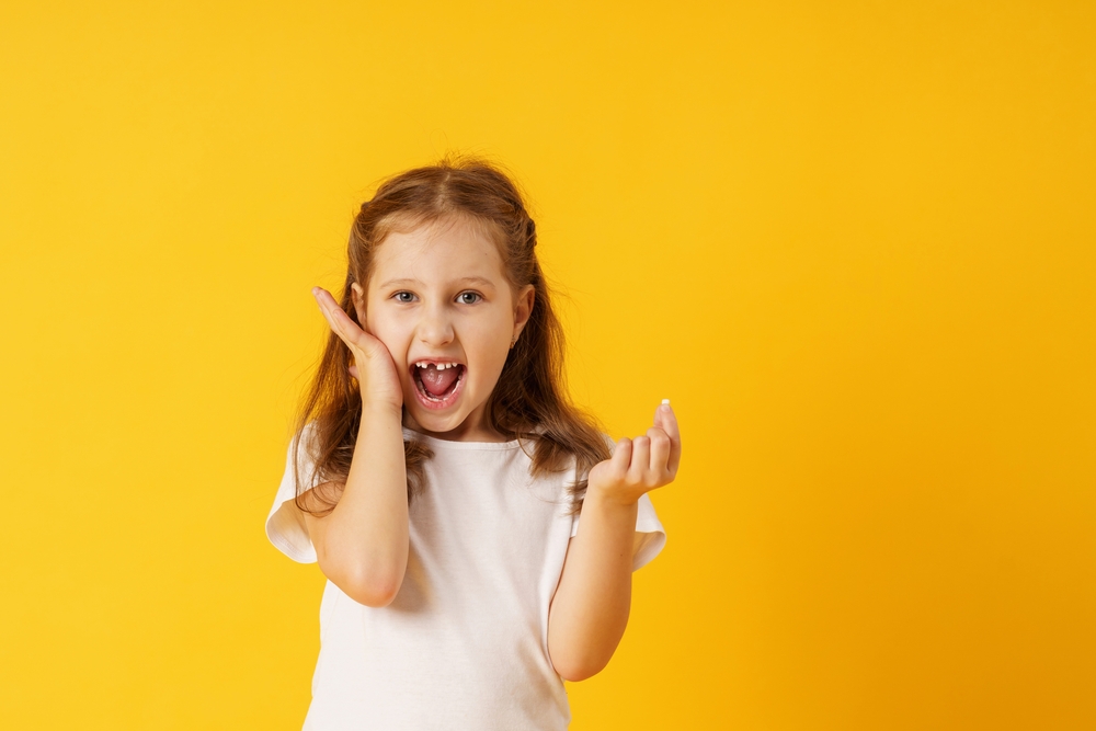 girl holds her first fallen baby tooth in her hand