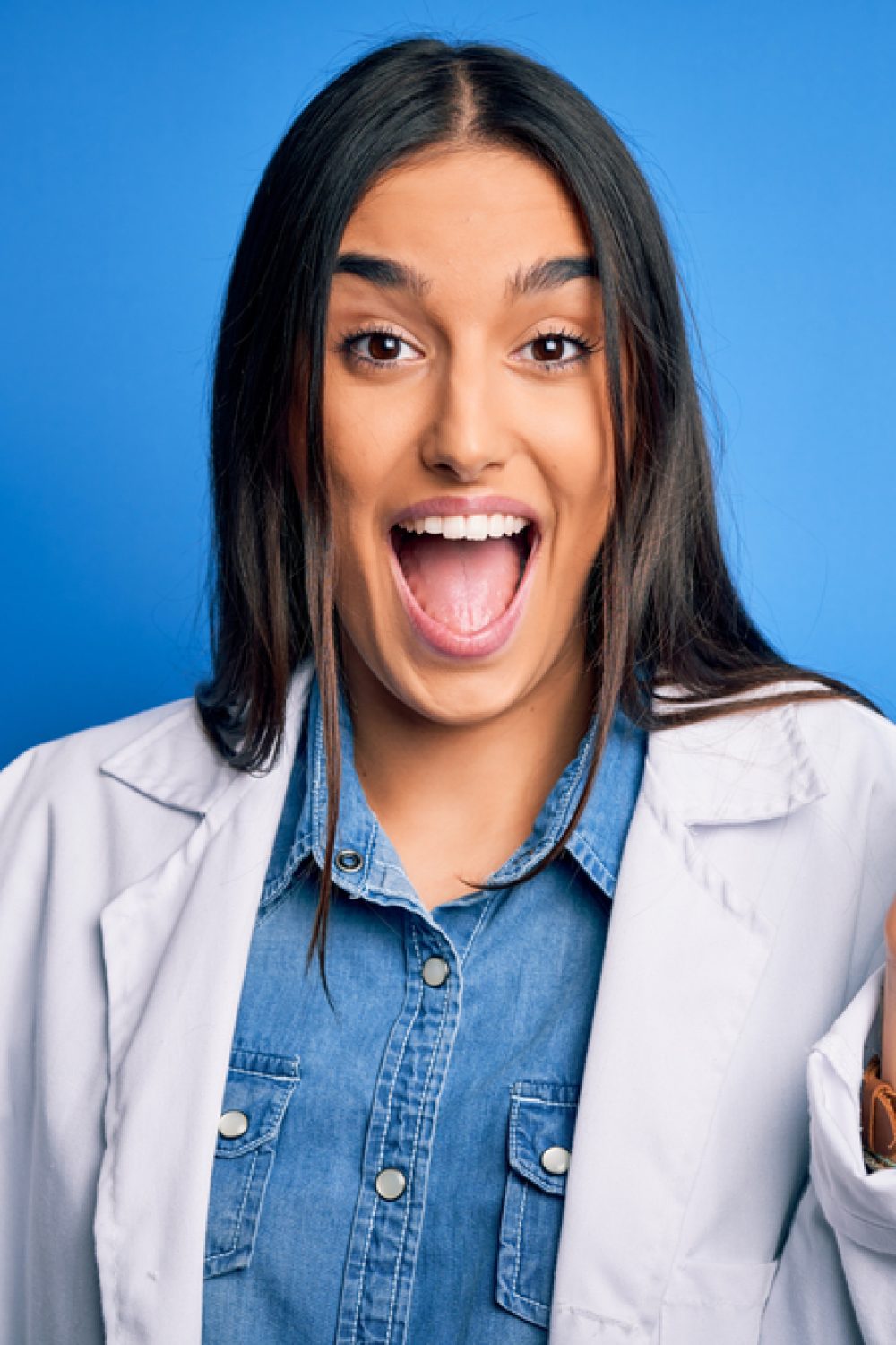 Young beautiful dentist woman wearing coat holding plastic teeth