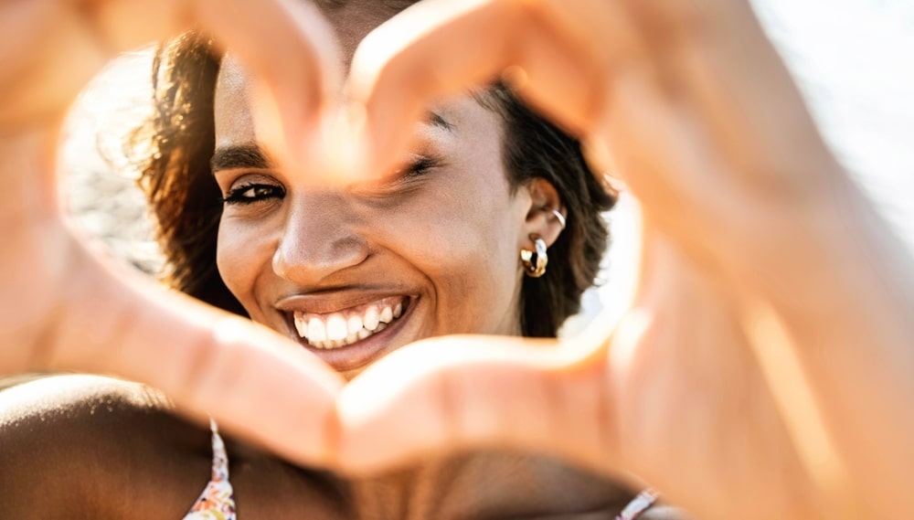 smiling woman in swimwear on the beach making a heart shape