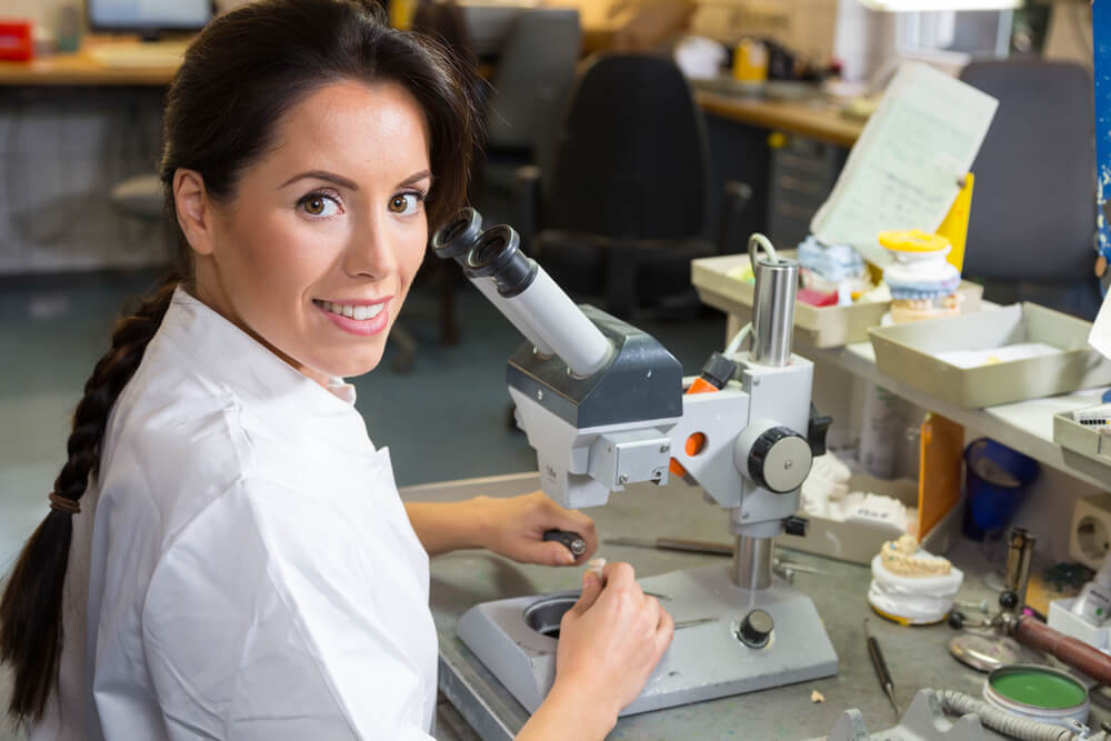 Technician in dental lab working on an implant under a microscope