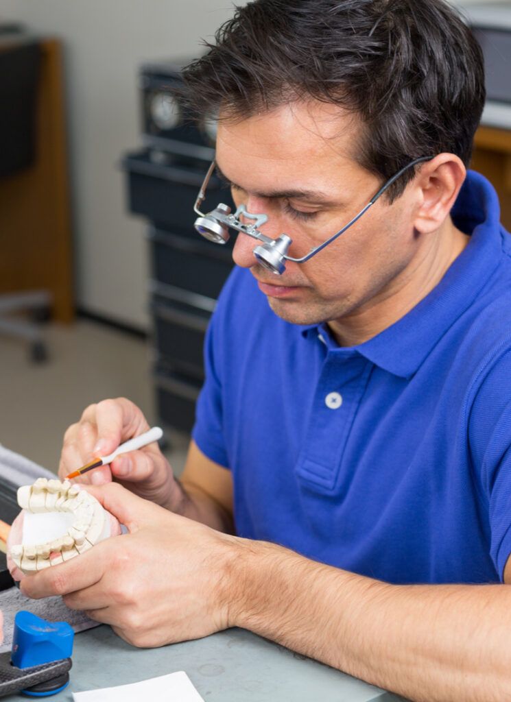 Dental lab technician with surgical loupes applying porcelain to dentition mold