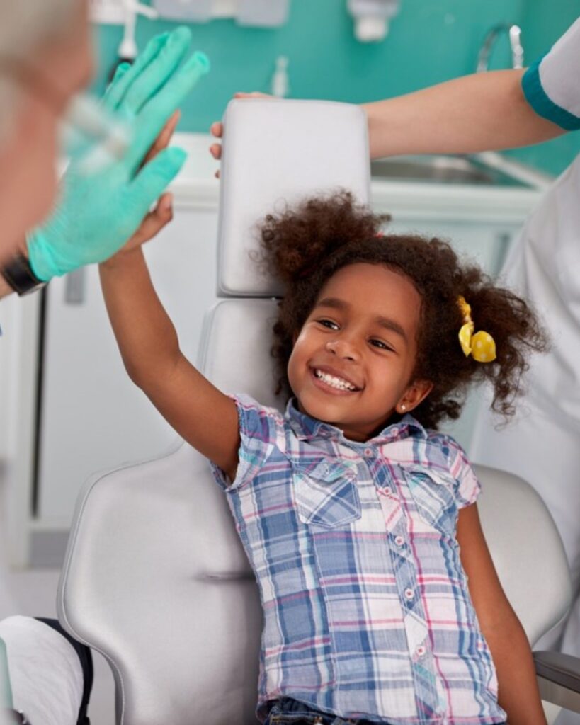 Lovely kid in dental chair with dentist satisfied after repairing teeth