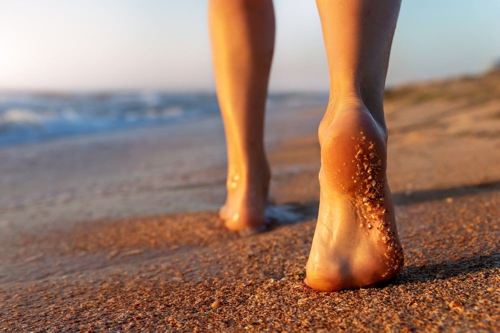 female person barefoot legs heel walking by scenic sandy ocean