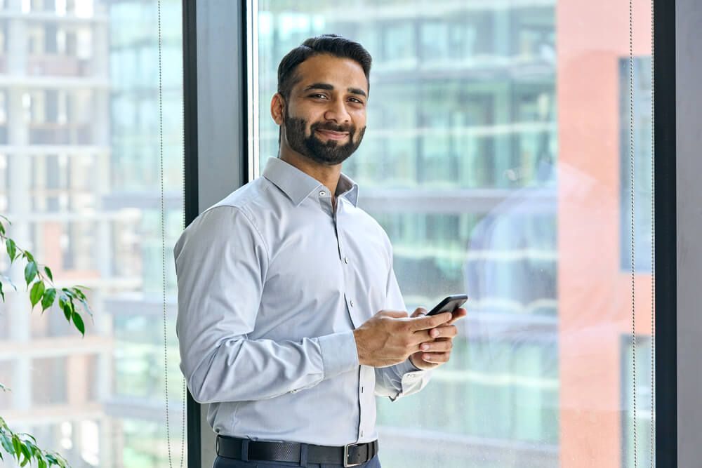 Smiling indian ceo businessman holding using cell phone