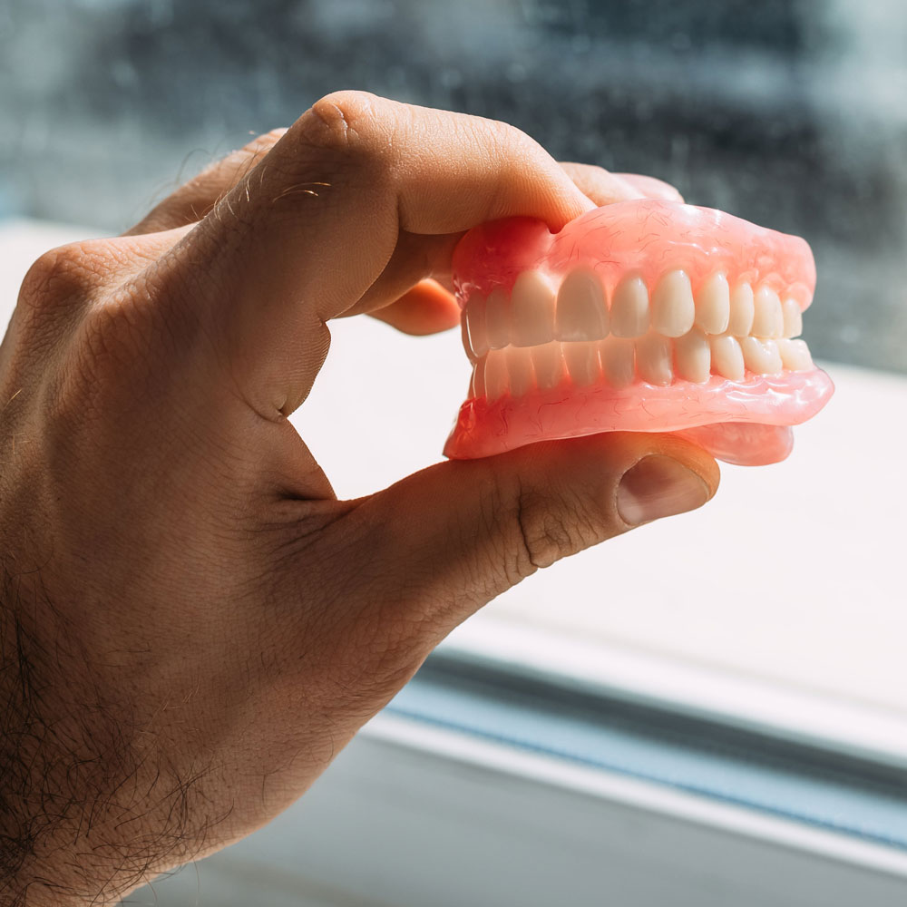 A man is holding dentures in his hands