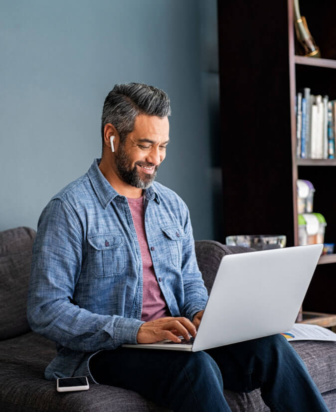 Successful mature indian businessman sitting on couch typing on laptop