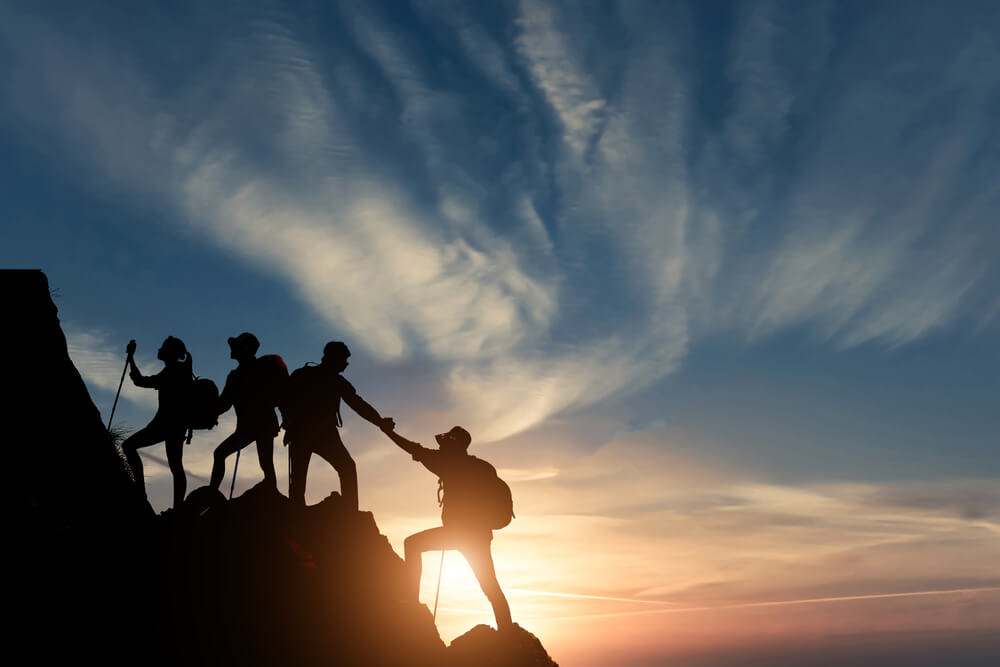 Silhouette male hiker groups celebrating success on top of a mountain.