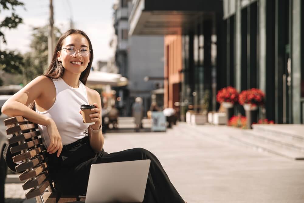 Asian brunette woman with wide smile sitting on bench