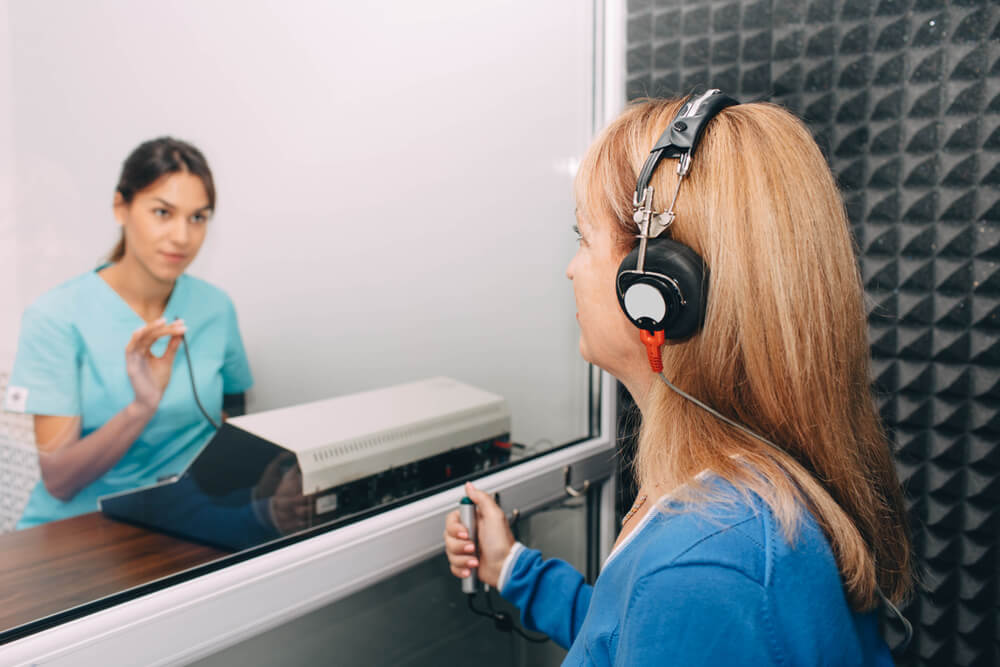 audiologist doing hearing exam to a mature patient using audiometer in special audio room.