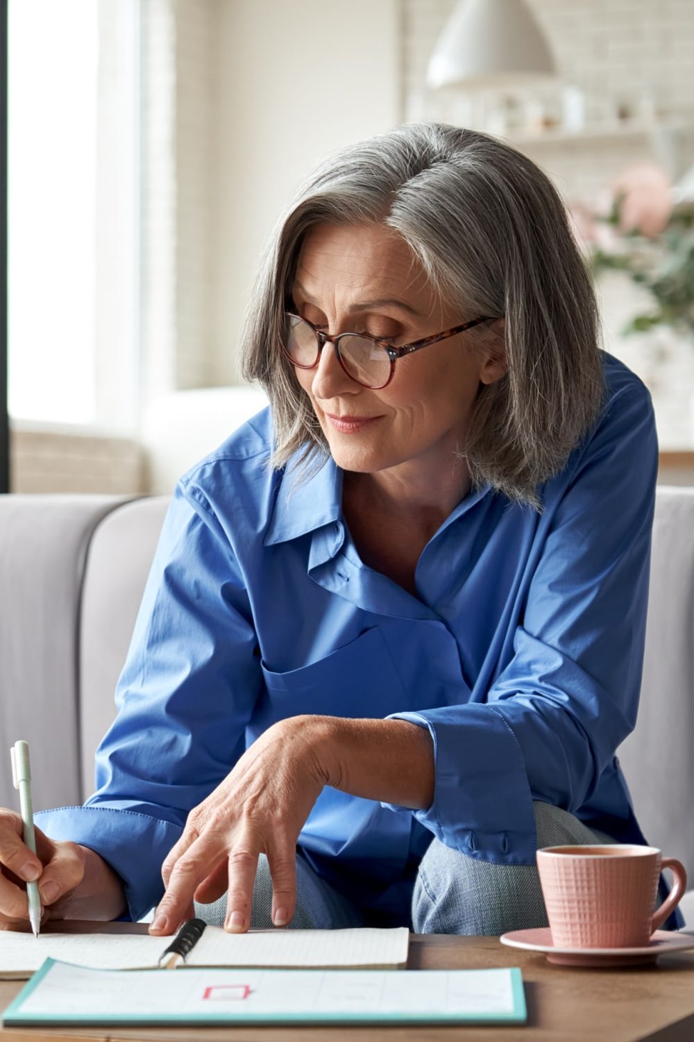 Happy stylish mature old woman remote working from home distance office on laptop taking notes.