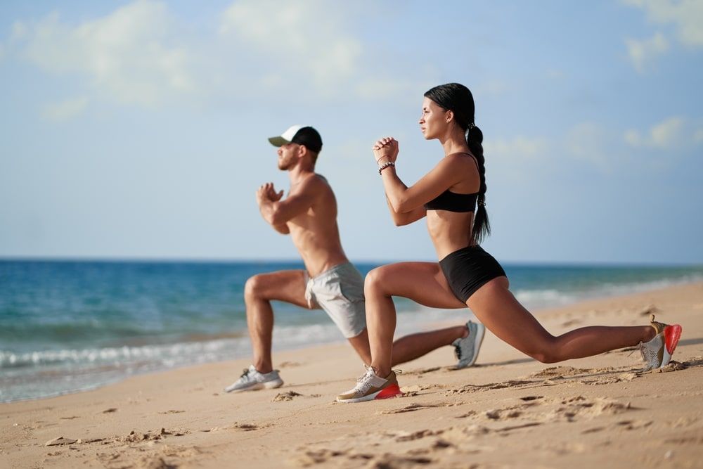 Young beautiful couple doing sports exercises at the beach.
