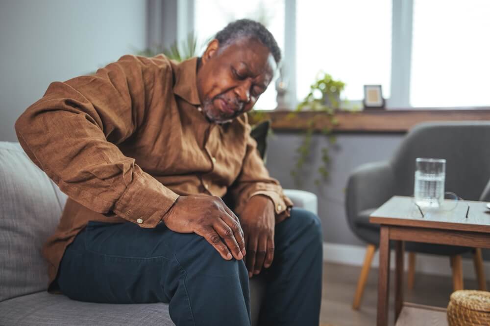 An African mature man suffers from knee pain while sitting