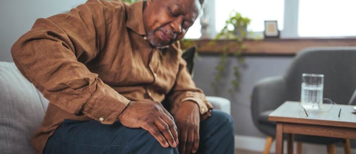 An African mature man suffers from knee pain while sitting