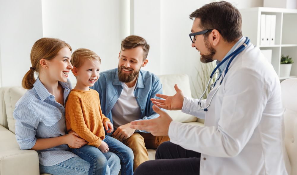 Positive male pediatrician talking with happy boy and parents during check up appointment