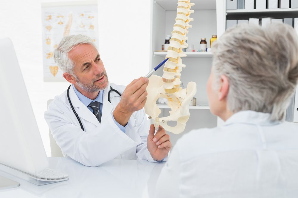 Male doctor explaining the spine to senior patient at desk in medical office