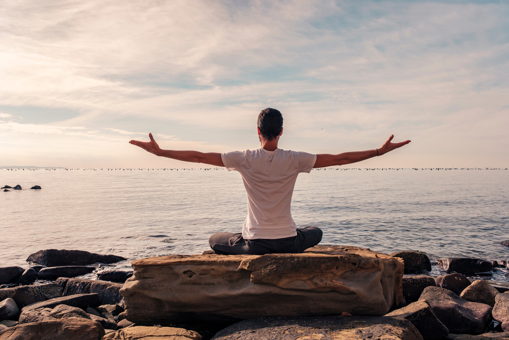 Attractive young man practicing yoga meditation and breathwork outdoors by the sea