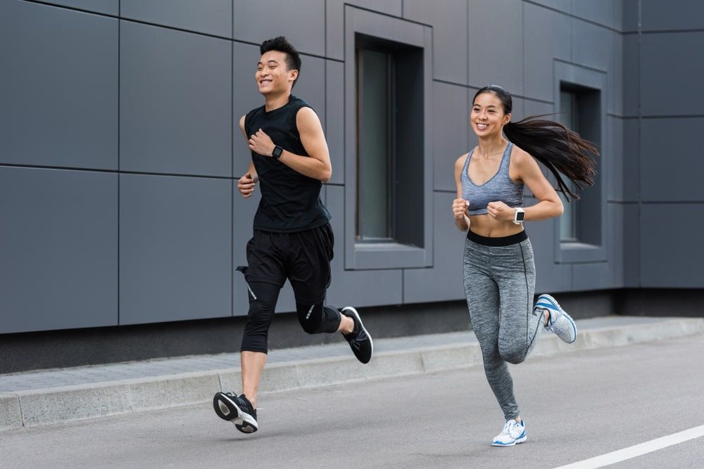 smiling female and male athletes running at urban street