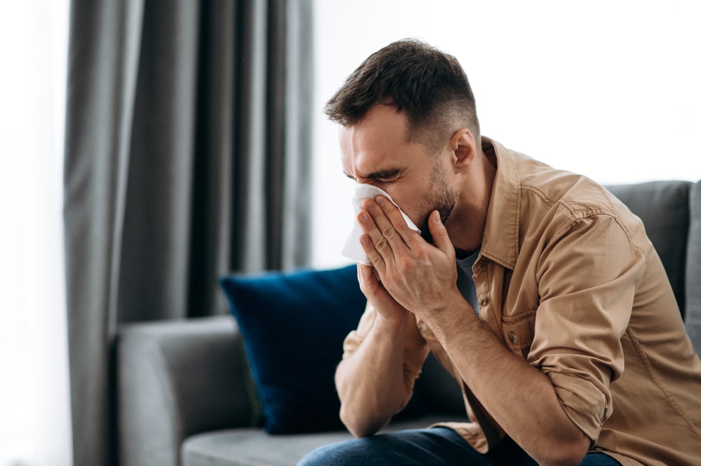 guy is sick with flu, he sneezes and blows his nose in a napkin