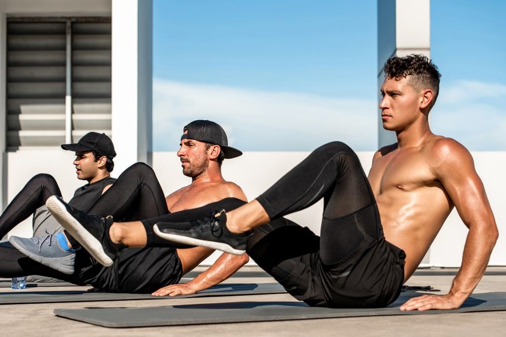 strong shirtless multiracial men doing bicycle crunches on mats