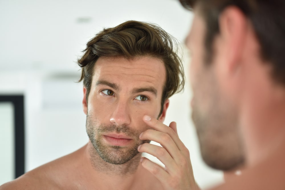 Handsome man applying facial cream in front of mirror