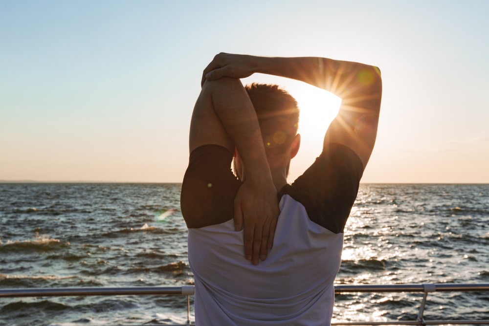 Back view of a sportsman stretching hands while standing at the beach