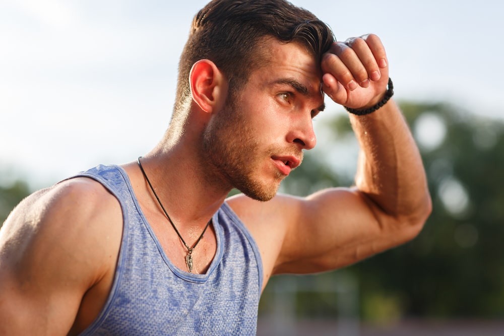 Young muscular sweaty man after workout outside on sunny day